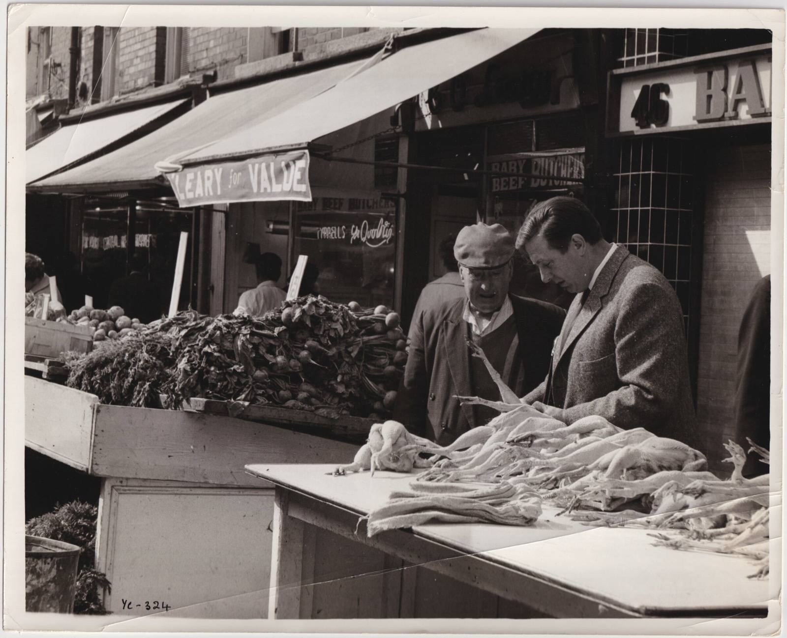 Two men at a street market poultry stall, examining birds laid out on a counter, in the early 1960s
